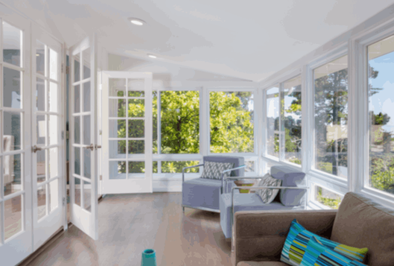 Bright sunroom with large glass windows, French doors, and a scenic ocean view