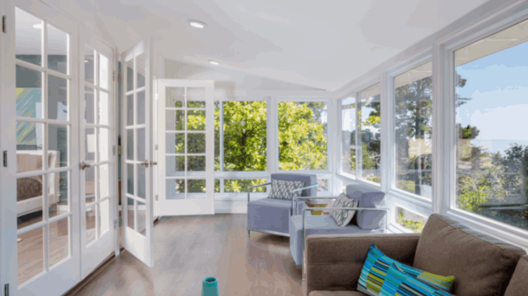 Bright sunroom with large glass windows, French doors, and a scenic ocean view