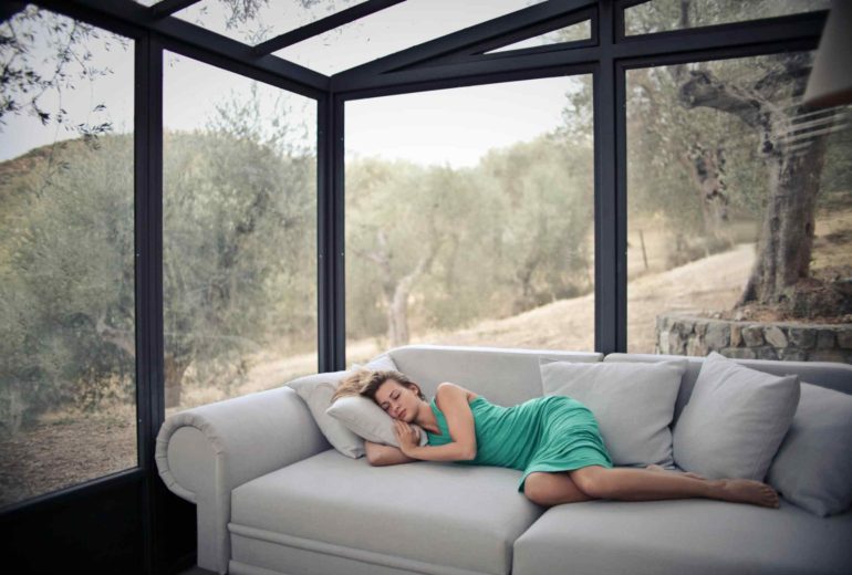 Woman relaxing on a sofa in a sunroom with floor-to-ceiling glass walls