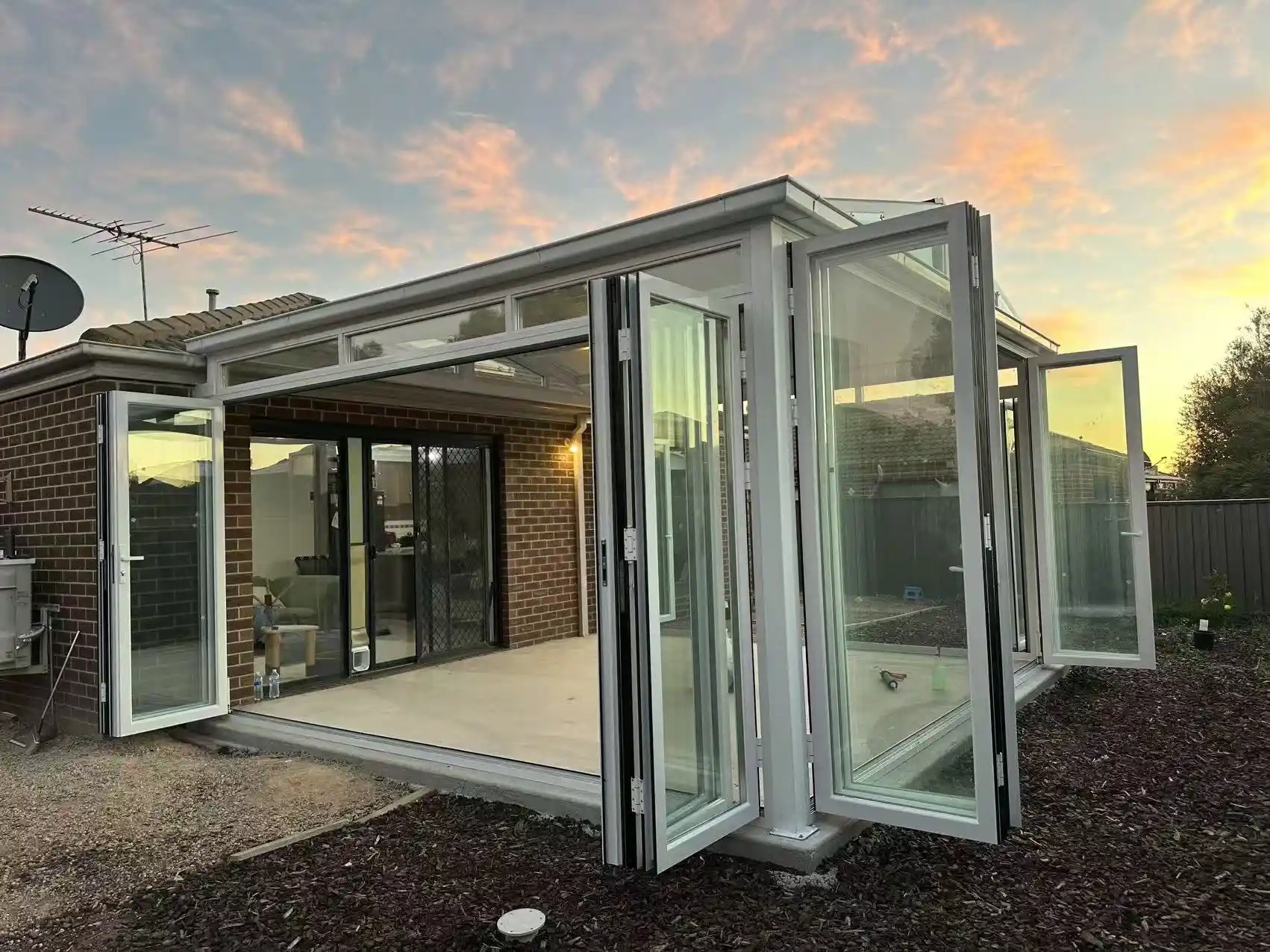 Glass sunroom with the bifold wall folded open onto the backyard