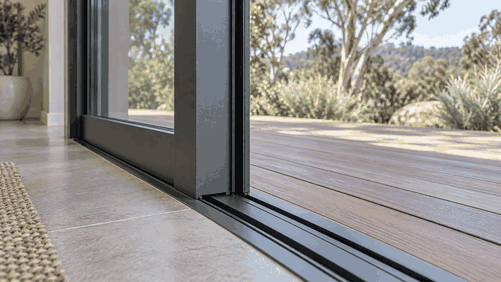 Bottom track of a black aluminium sliding door at a timber deck threshold, showing a clean precisely fitted track with no vertical play