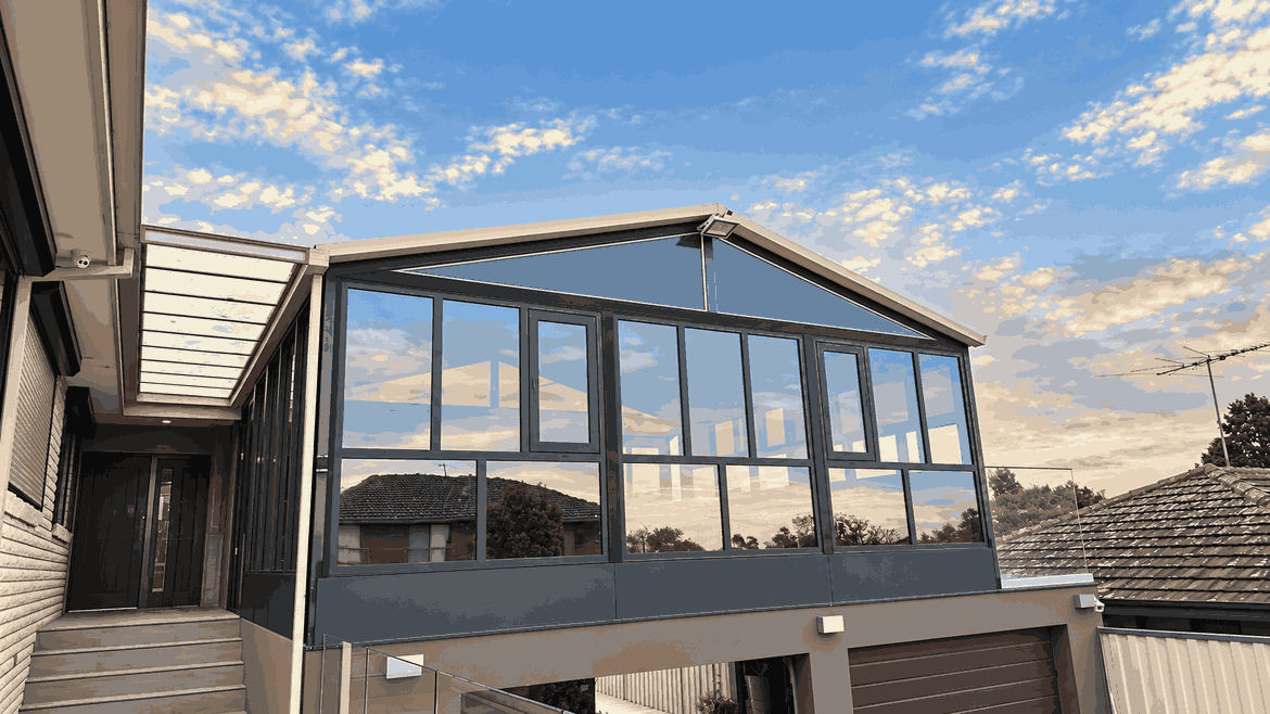 Glazed upper-level sunroom extension built above a garage, photographed at dusk