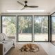 Golden retriever asleep on a rug in a sunroom on a hot summer day, ceiling fan and skylight overhead, glass doors open to a timber deck